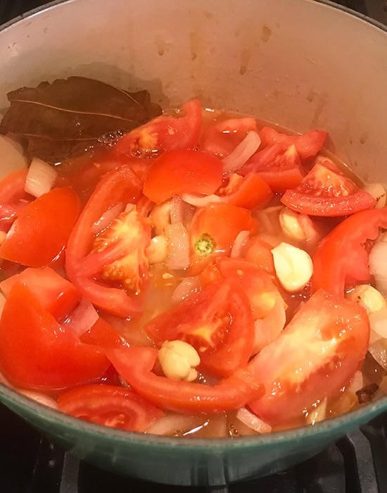 chopped onions with whole spices and chopped tomatoes in a dutch oven