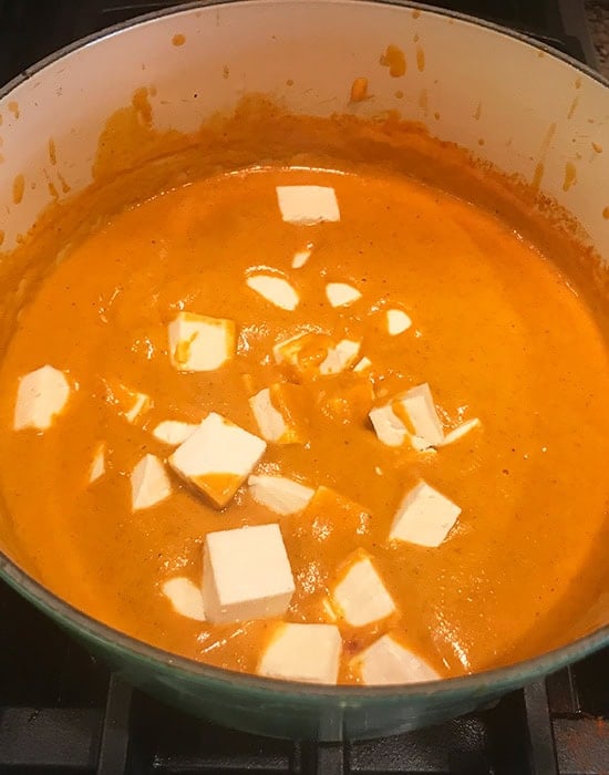 cubes of paneer being added to a pot of curry