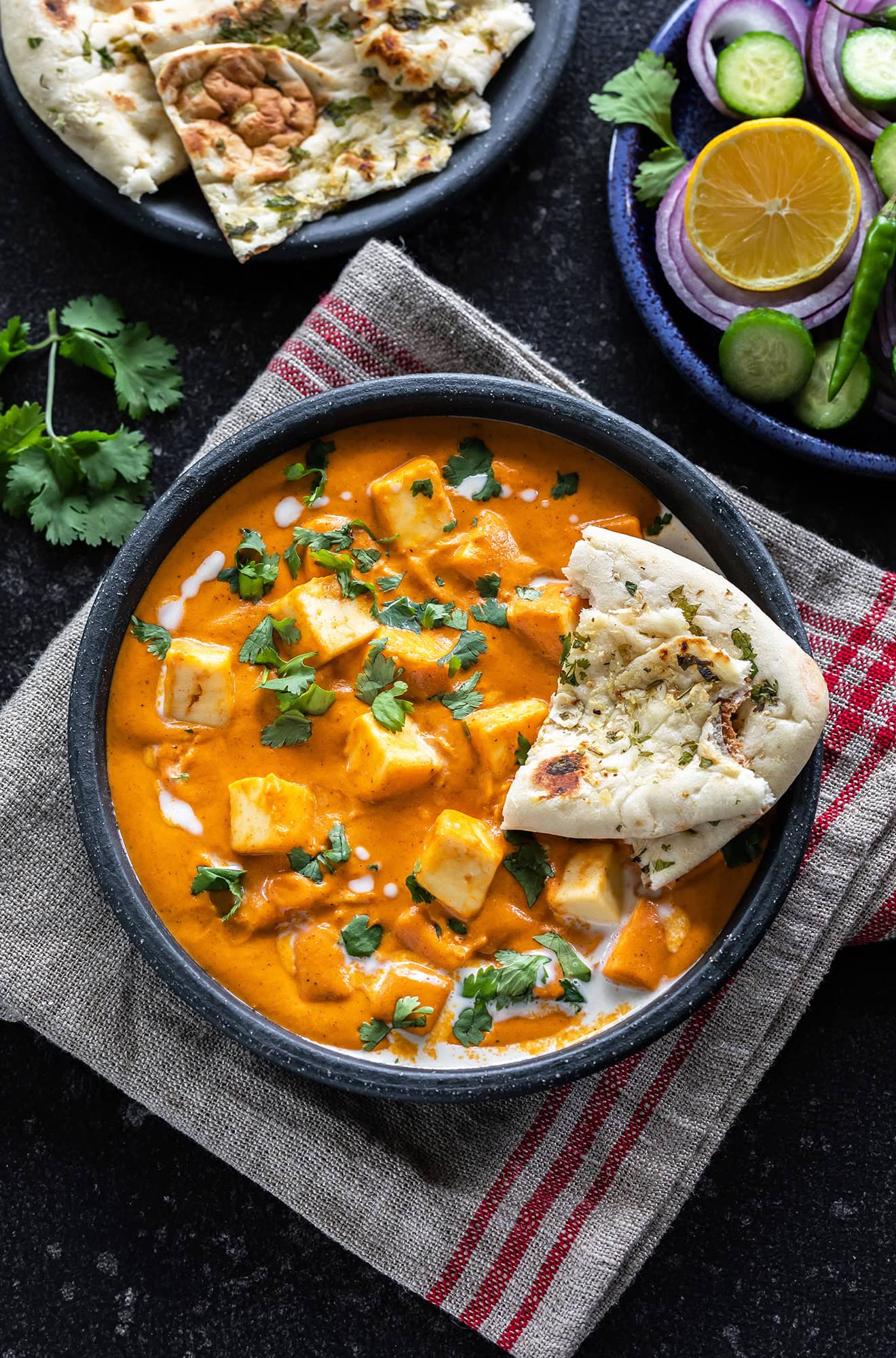 bowl of paneer butter masala served with a piece of naan and garnished with cilantro and cream