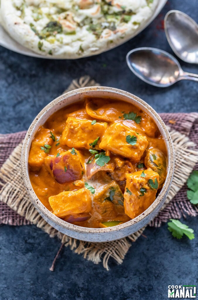 paneer curry served in a white bowl garnished with cilantro with naan in the background