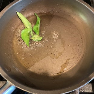 a small pan with oil, mustard seeds and curry leaves