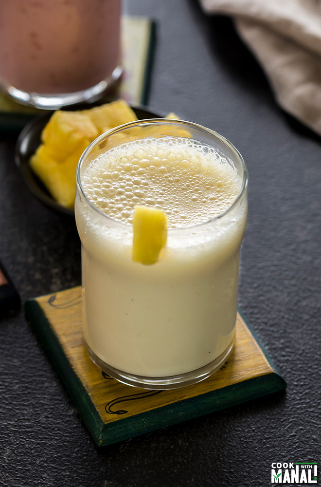 glass of pineapple ginger lassi on a coaster with more glasses of lassi in the background