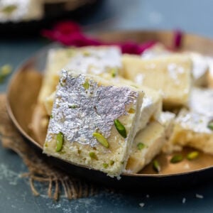 a piece of burfi placed in a golden bowl with more burfi in the back