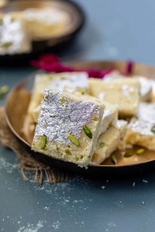 a piece of burfi placed in a golden bowl with more burfi in the back