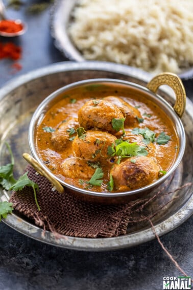 dum aloo served in a copper kadai garnished with cilantro with a plate of rice in the background