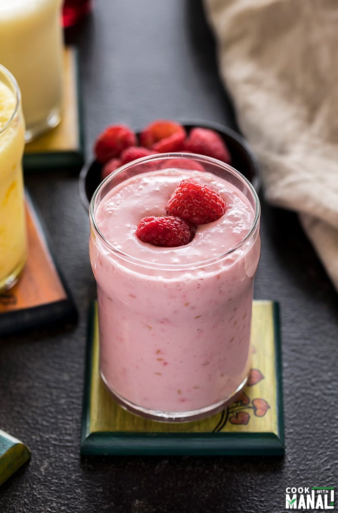 glass of raspberry coconut lassi on a coaster with more glasses of lassi in the background
