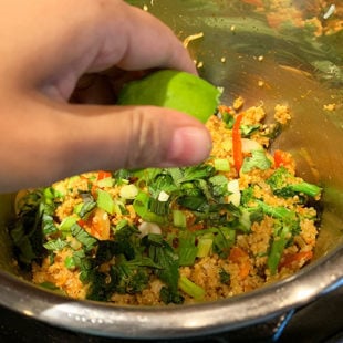hand squeezing lime juice in a pot full of veggies and quinoa