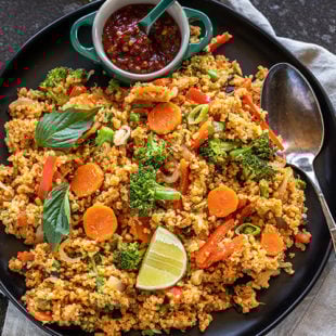 quinoa with veggies and lime wedge served in a plate with bowl of hot sauce on side