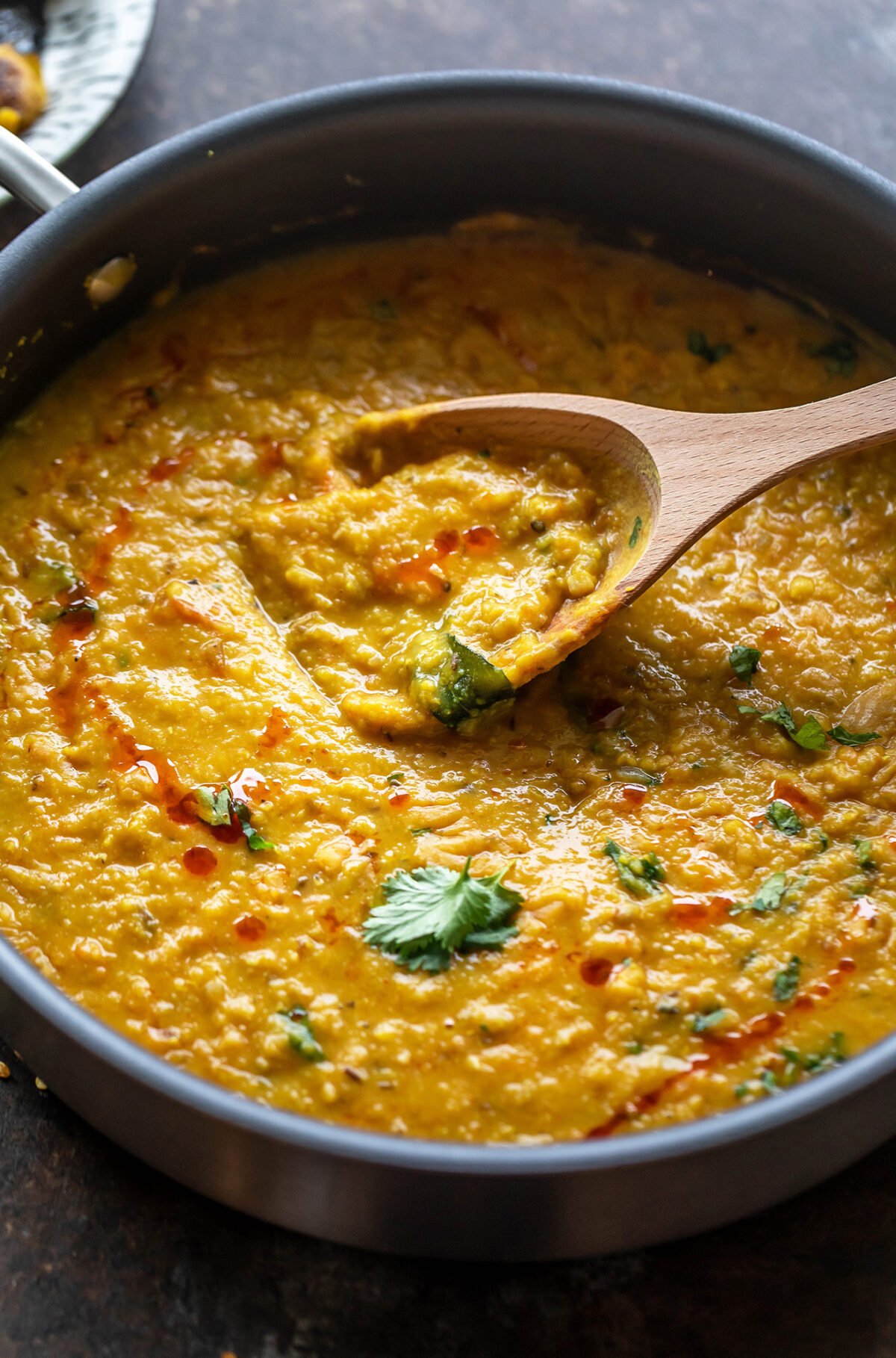 dal topped with cilantro in a pan with a wooden spatula place on the side
