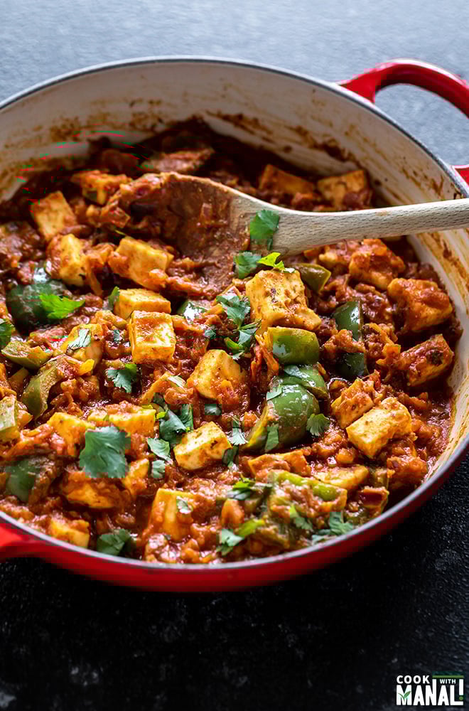 kadai paneer in a red color wok with a wooden spatula with blue napkin in the background