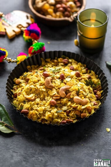roasted poha chivda served in black rimmed plate with a candle lit in the background and some curry leaves on the side