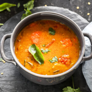 sambar served in a grey bowl garnished with curry leaves with twigs on cilantro and more curry leaves scattered all around