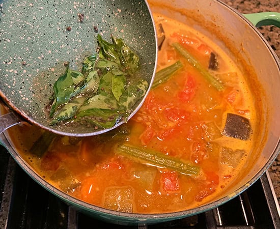 tadka from small pan being poured into pot of dal