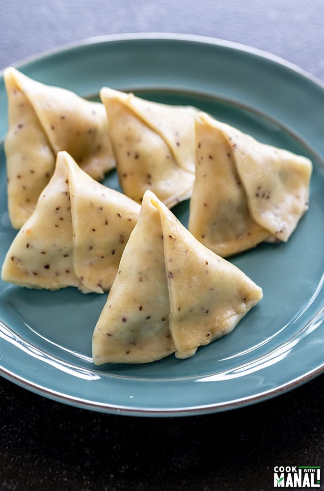 five pieces of uncooked samosa lined in a plate