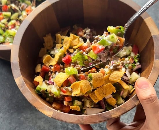 a spoon scooping the salad from a large wooden bowl