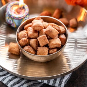 shakarpara in a kansa bowl with a lighted diya in the back