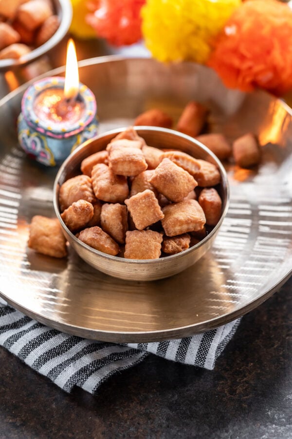 shakarpara in a kansa bowl with a lighted diya in the back