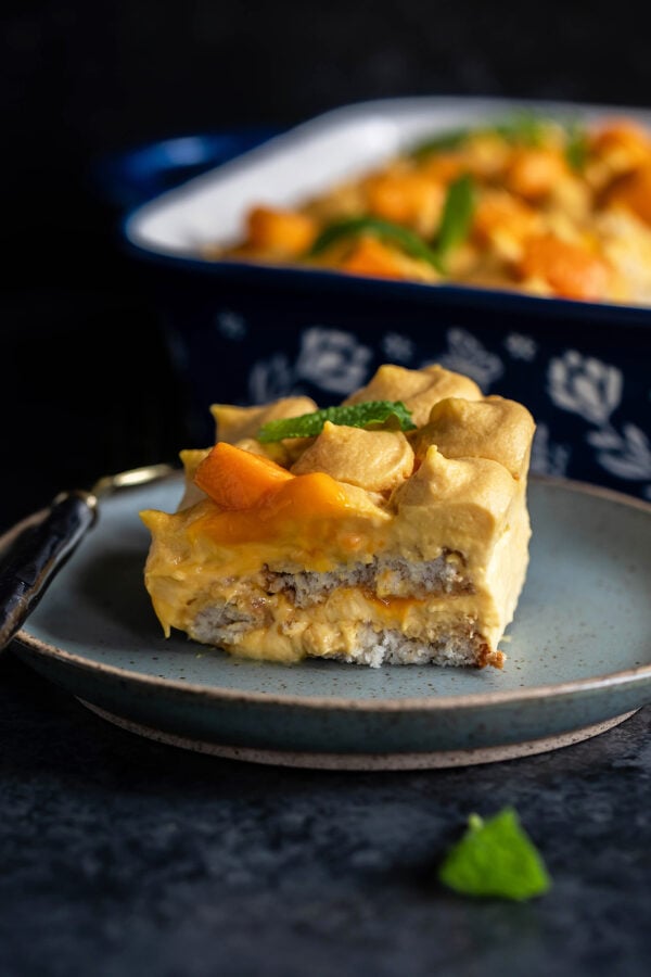 slice of mango tiramisu served in a blue plate with a fork placed on the side