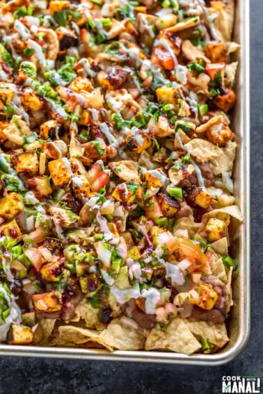 a full sheet of nachos topped with paneer, cheese, onion, tomato, cilantro