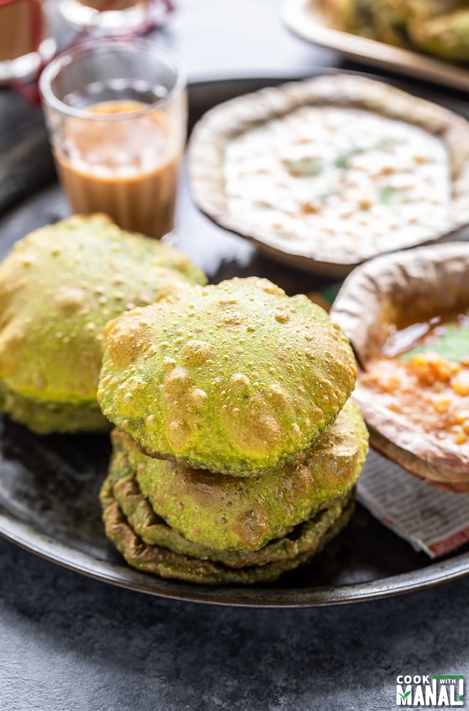 stack of puris placed in a plate along with glass of chai and bowls of curry and raita