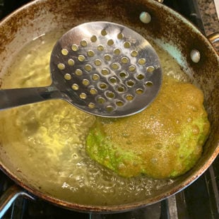 puri having browned spots on top being fried in hot oil