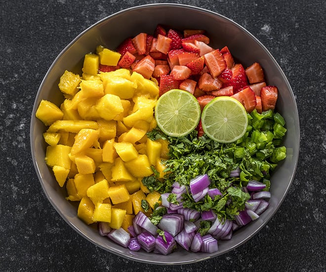 a large bowl with diced mangoes, strawberries, onion, jalapeƱo, cilantro and cut lime