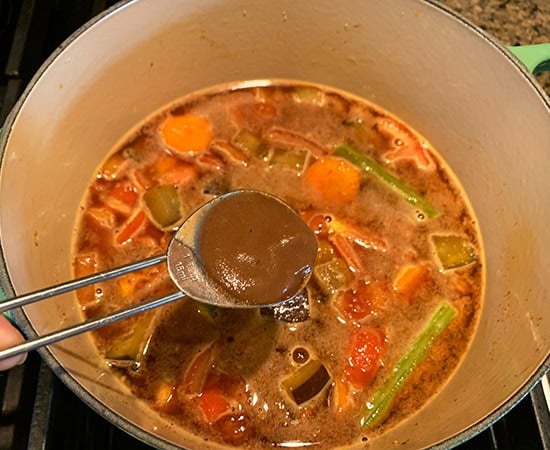 tamarind pulp being added to a pot of veggies