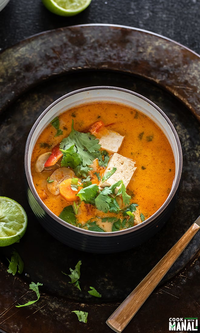 vegan thai curry soup served in a black bowl garnished with cilantro and lime wedges on the sides