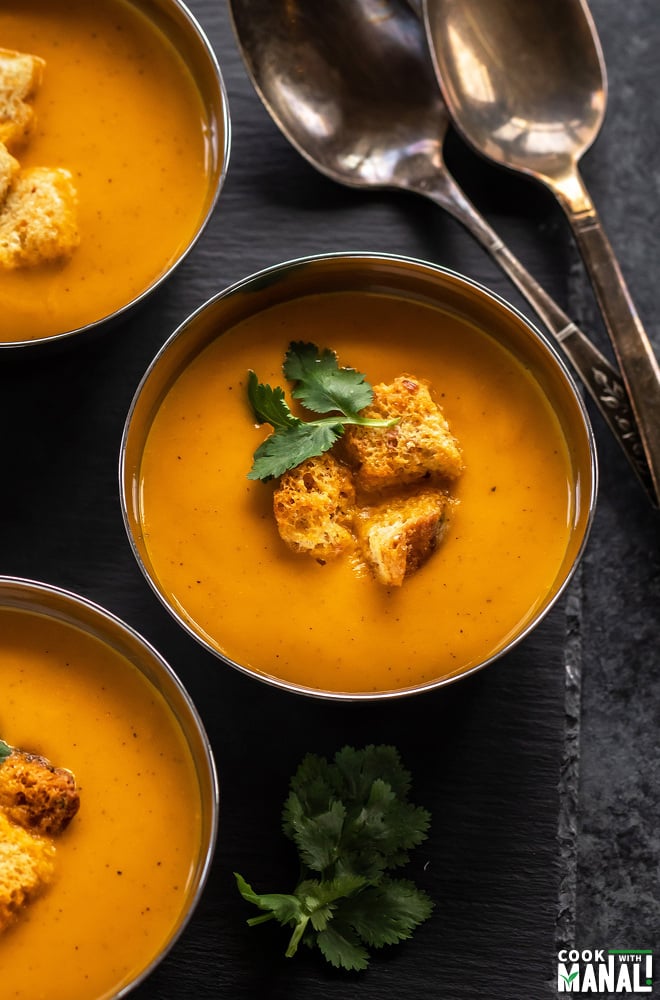 bowls of tomato soup topped with croutons and cilantro