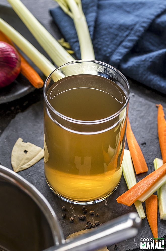 vegetable stock in a glass container with veggies on the side
