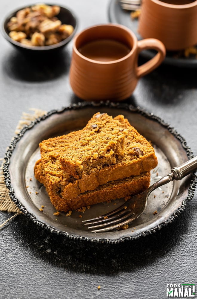 stack of atta jaggery cake with the top sliced cut in half and cups of chai in the background
